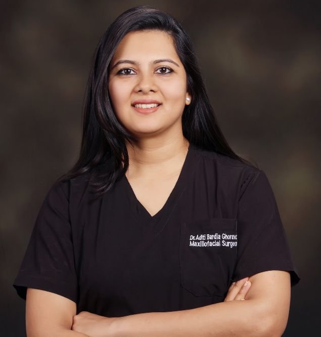 "Professional portrait of a maxillofacial surgeon in black scrubs, smiling confidently with arms crossed."