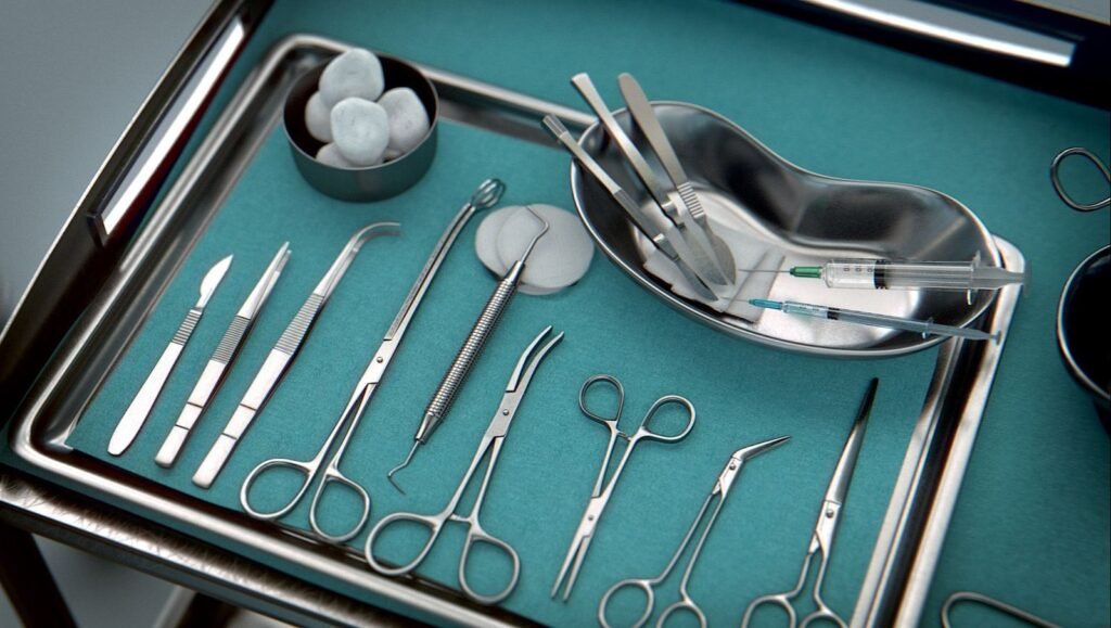 A close-up photo of a surgical tray on a blue cloth, containing various metallic surgical instruments including scalpels, forceps, scissors, a retractor, a syringe, and cotton balls in a basin.